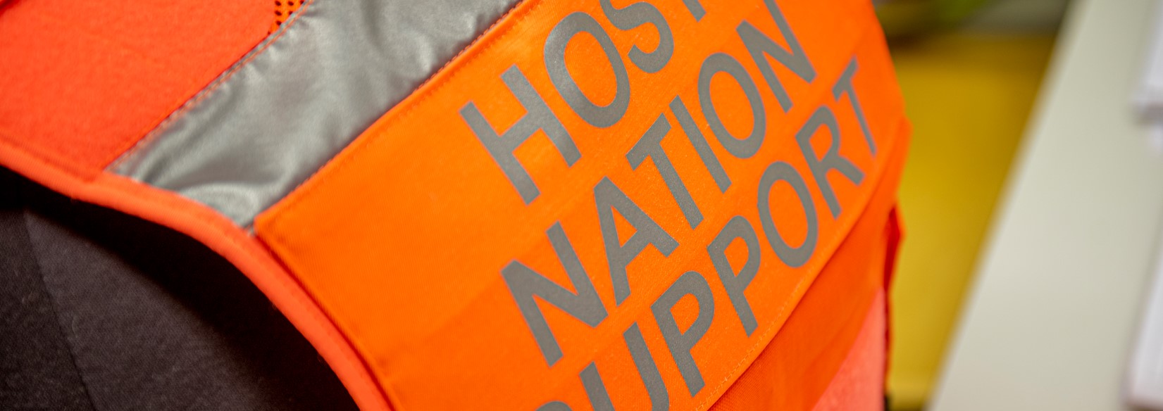 Oranssi heijastinliivi, jossa lukee Host Nation Support