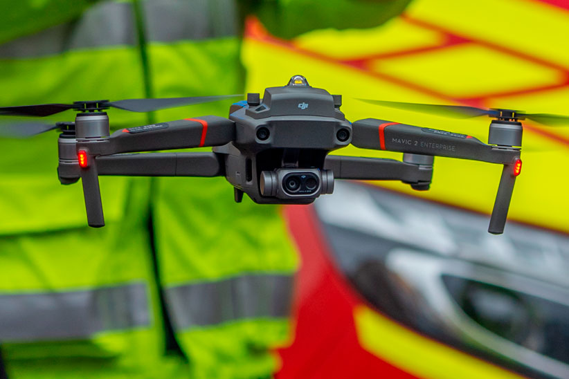 Harmaa drone lentää matalalla ilmassa. Taustalla palomestari.