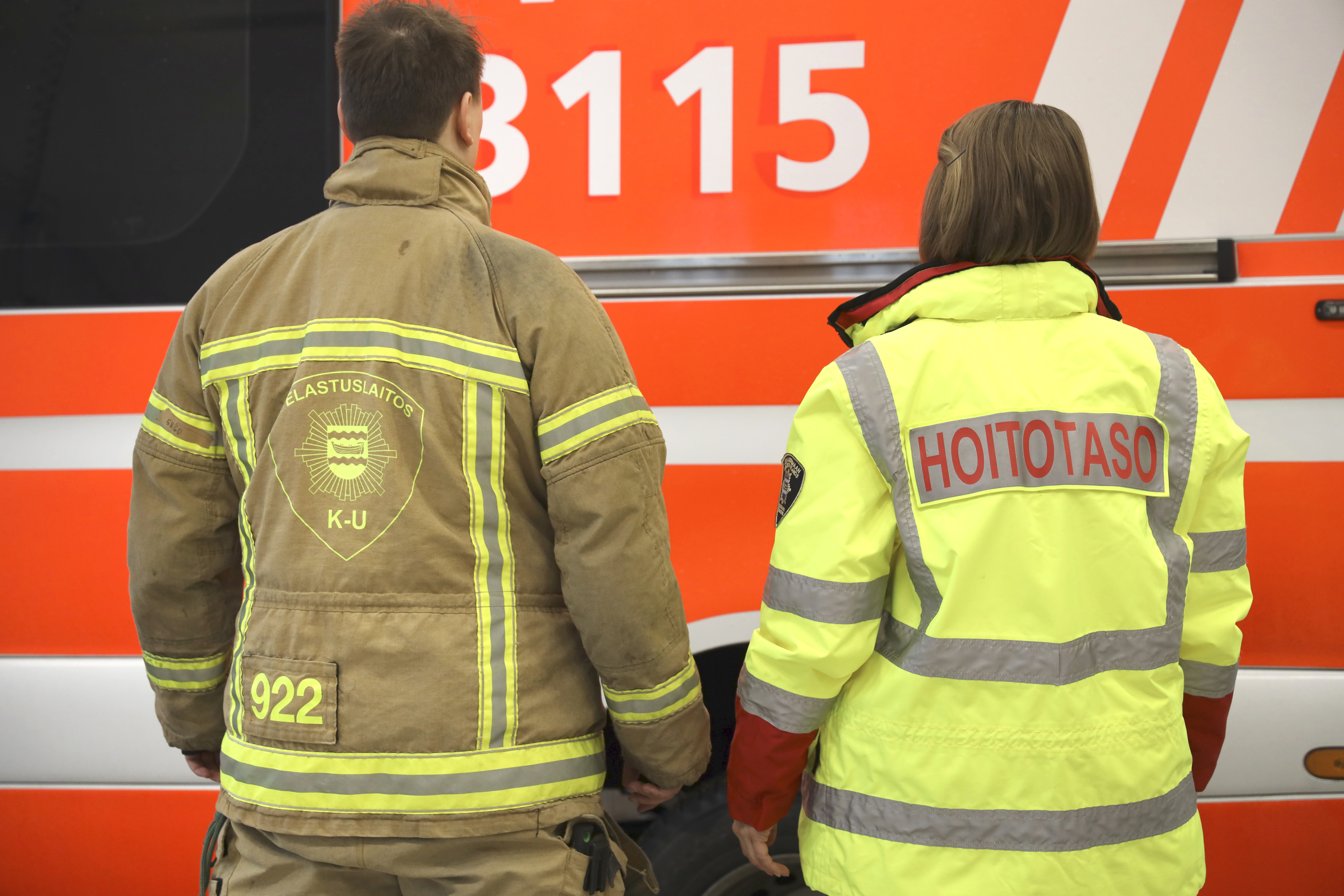 Palomiehen ja ensihoitajan selät ja taustalla pelastusyksikkö.