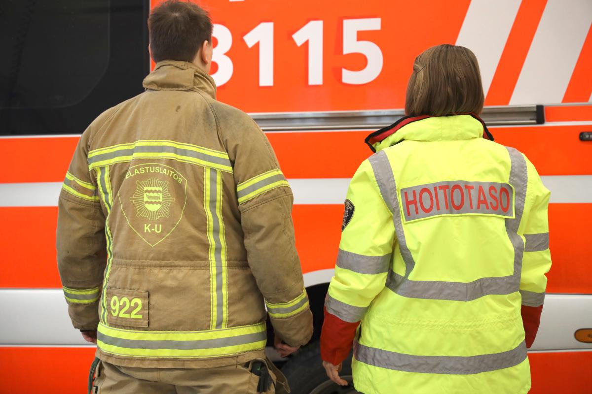 Palomiehen ja ensihoitajan selät ja taustalla pelastusyksikkö.